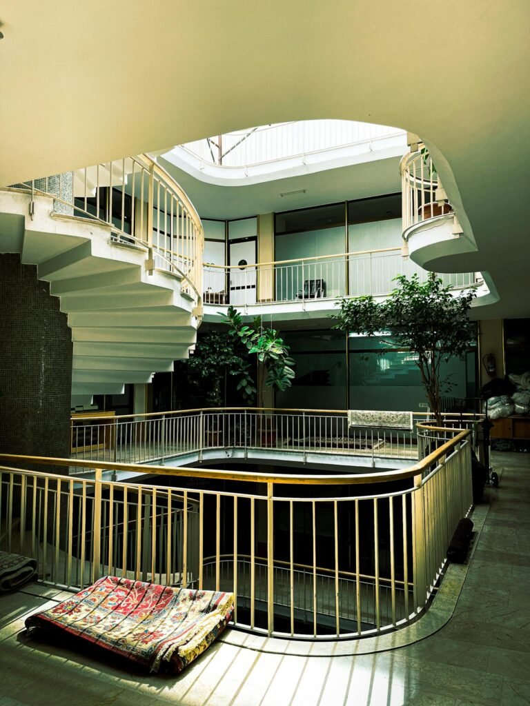 A modern spiral staircase with railings in a sunlit atrium featuring sleek design and interior greenery.
