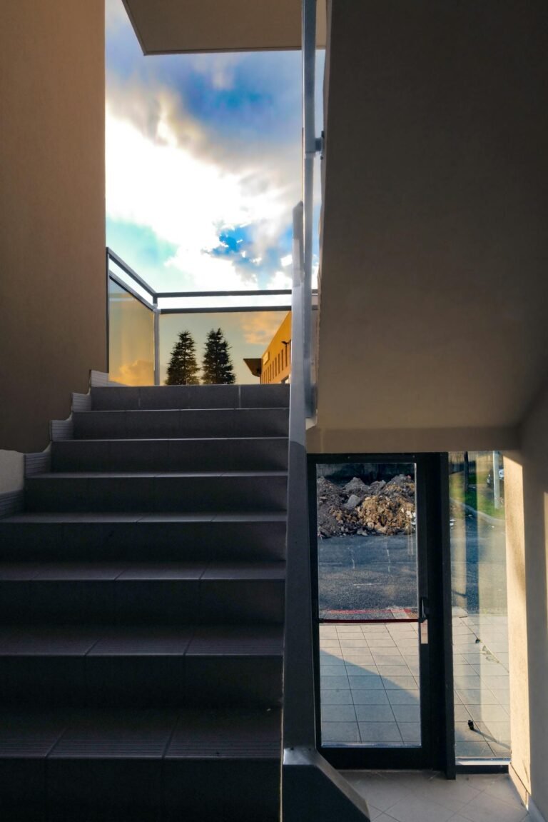 Minimalist staircase with glass railings offering a view of the sky and outdoors, capturing sunset tones.